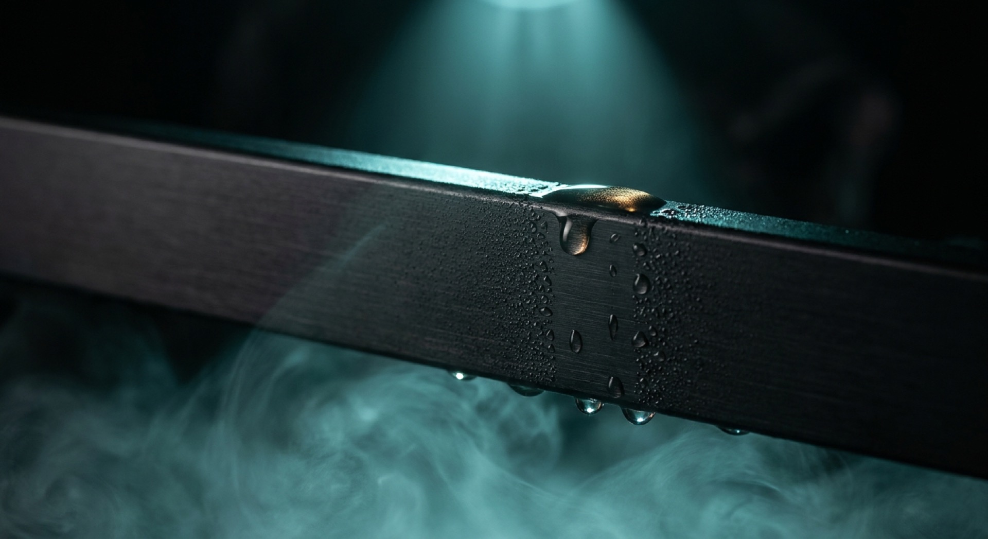 Condensation droplets forming on a brushed-black surface in atmospheric teal mist